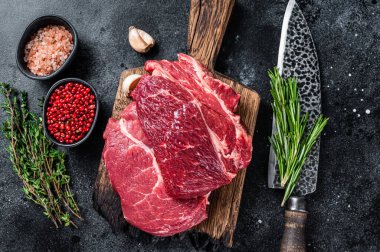 Çiğ Chuck 'ın gözü siyah Angus bifteği kasap tahtasının üzerinde bıçakla yuvarlandı. Siyah arka plan. Üst görünüm