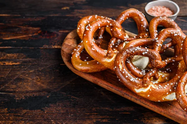 Pretzels macios caseiros com sal em uma placa de madeira. Fundo de madeira escuro. Vista superior. Espaço de cópia — Fotografia de Stock