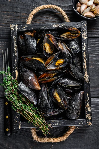 Kabuklu midyeler ahşap bir tepside otlarla birlikte. Siyah ahşap arka plan. Üst görünüm