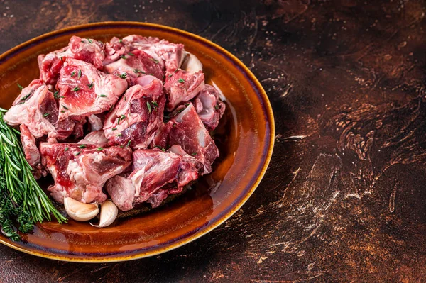 Carne de cordero cruda cortada en cubitos para gulash o guiso con hueso en un plato rústico. Fondo oscuro. Vista superior. Copiar espacio —  Fotos de Stock