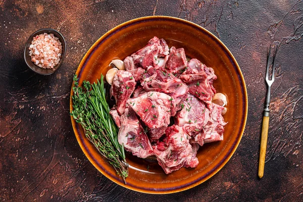 Carne di montone cruda tagliata a dadini per gulasch o stufato con osso su un piatto rustico. Sfondo scuro. Vista dall'alto — Foto Stock