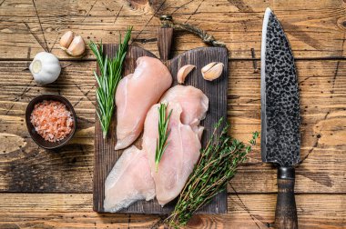 Taze kesilmiş tavuk göğsü fileto bifteği ahşap kesme tahtasının üzerinde mutfak bıçağıyla. Ahşap arka plan. Üst görünüm