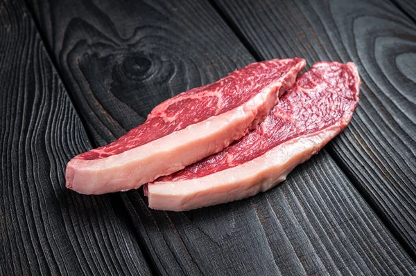 Syrový hovězí steak nebo hovězí steaky se svíčkovou na řeznickém stole. Černé dřevěné pozadí. Horní pohled — Stock fotografie