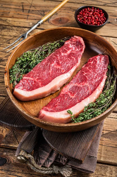 Biftecks de viande de bœuf crus dans une assiette en bois aux herbes. fond woden. Vue du dessus — Photo