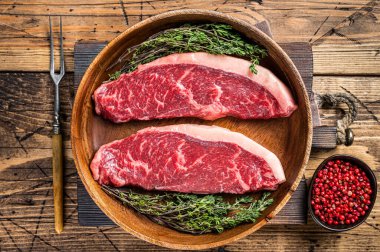 Pişmemiş çiğ sığır filetosu sığır eti bifteği ahşap bir tabakta otlarla birlikte. woden arka plan. Üst görünüm