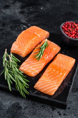 Misket tahtasında çiğ somon filetosu ve şifalı otlar. Siyah arka plan. Üst görünüm