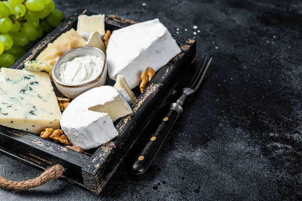 Prato de queijo variado com Brie, Camembert, Roquefort, parmesão, queijo creme azul, uva e nozes. Fundo preto. Vista superior. Espaço de cópia — Fotografia de Stock