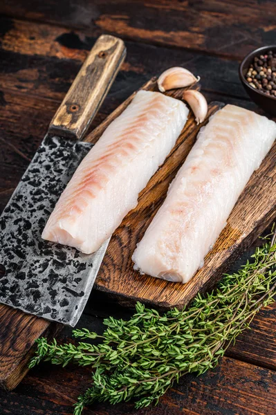 Filetto di baccalà crudo su tavola di legno con mannaia da macellaio. Fondo in legno scuro. Vista dall'alto — Foto Stock