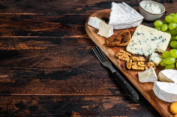 Placa de queijo variada com Brie, Camembert, Roquefort, parmesão, queijo creme azul, uva e nozes. Fundo de madeira escuro. Vista superior. Espaço de cópia — Fotografia de Stock