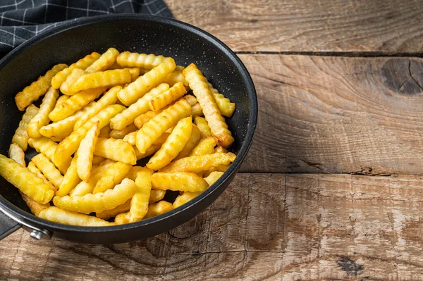 Fried Crinkle oven French fries potatoes sticks in a pan. Wooden background. Top view. Copy space — Stock Photo, Image