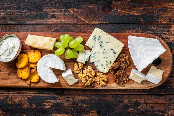 Sortierte Käseplatte mit Brie, Camembert, Roquefort, Parmesan, blauem Frischkäse, Trauben und Nüssen. Dunkler Holzhintergrund. Ansicht von oben — Stockfoto