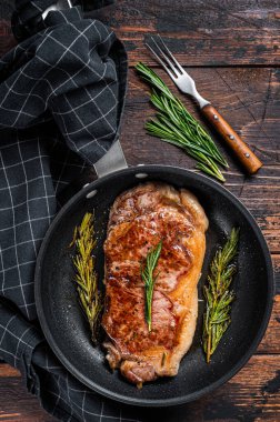 Tavada ızgara çizgili biftek ve otlar. Koyu ahşap arka plan. Üst görünüm