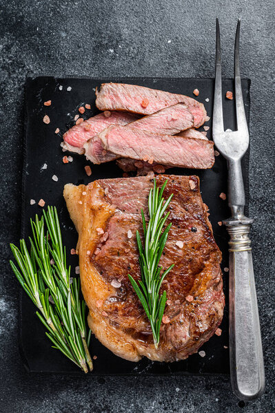 Cut roasted new york strip beef meat steak or striploin on a marble board. Black background. Top view.