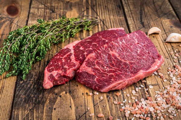 Raw denver or top blade meat steak on a butchery table with herbs. wooden background. Top view