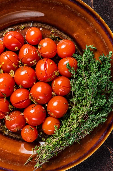 Маринованные помидоры черри в деревенской тарелке с чесноком и тимьяном. Темный фон. Вид сверху — стоковое фото