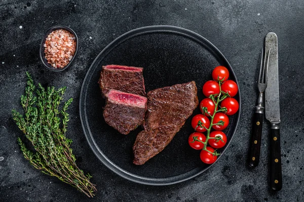 Rostad styckad nötköttstek på en tallrik med timjan. Svart bakgrund. Ovanifrån — Stockfoto