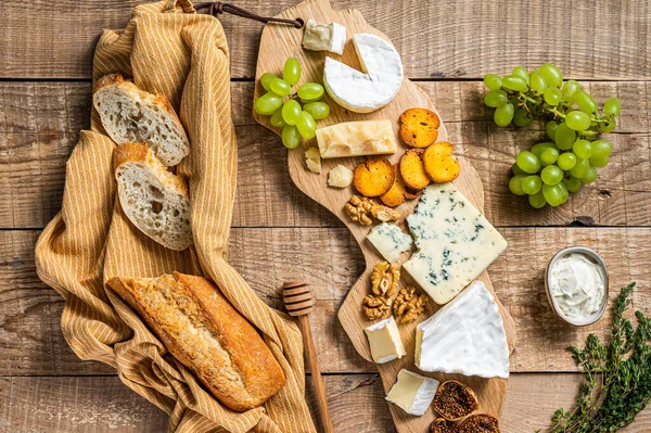 Tábua de queijo. Brie, Camembert, Roquefort, parmesão e creme de queijo azul com uva, figo, pão e nozes em tábua de madeira. fundo de madeira. Vista superior — Fotografia de Stock