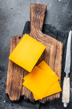 Tahta kesme tahtasının üzerinde Cheddar Cheese dilimleri. Siyah arka plan. Üst görünüm