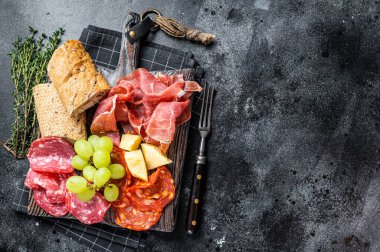Soğuk et tabağı, şarküteri, tahtadan yapılmış ekmek ve üzümlü geleneksel İspanyol mezeleri. Siyah arka plan. Üst Manzara. Boşluğu kopyala