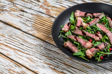 Dilimlenmiş biftek ve roka yapraklı salata. Beyaz ahşap arka plan. Üst Manzara. Boşluğu Kopyala
