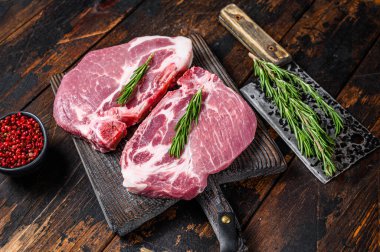 Et satırıyla kesme tahtasının üzerinde otlu çiğ domuz filetosu bifteği. Koyu ahşap arka plan. Üst görünüm