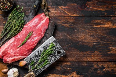 Kesme tahtasının üzerinde satırla birlikte çiğ etekli biftek. Koyu ahşap arka plan. Üst Manzara. Boşluğu kopyala