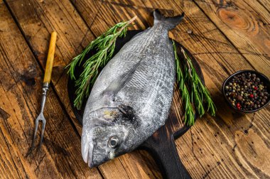 Çiğ deniz kepeği ya da kesme tahtasındaki baharat ve otlu dorado balığı. Ahşap arka plan. Üst görünüm