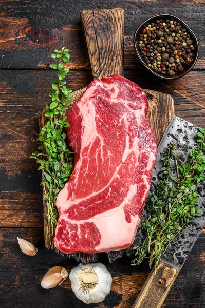 Raw Black Angus prime beef chuck roll steak op een snijplank met hakmes. Donker houten achtergrond. Bovenaanzicht — Stockfoto