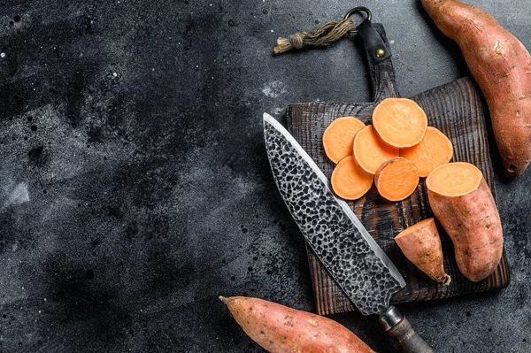 Raw cut batata Sweet potato on Wooden cutting board. Black background. Top view. Copy space