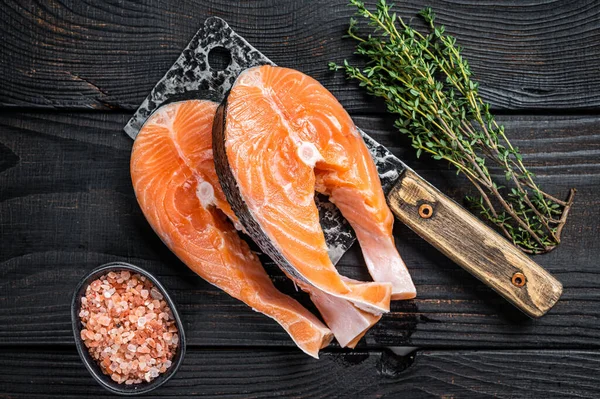 Bistecche fresche di salmone crudo sulla mannaia del macellaio. Fondo in legno nero. Vista dall'alto — Foto Stock