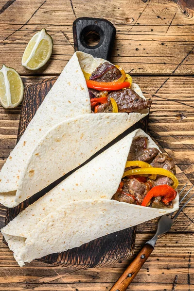 Fajitas Tortilla envelopper avec des rayures de viande de bœuf, poivron de couleur et oignons et salsa. Fond en bois. Vue du dessus — Photo