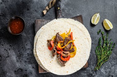 Meksika Fajitası, renkli biber ve soğanlı, tortilla ve salsa ile servis ediliyor. Siyah arka plan. Üst görünüm