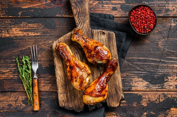 BBQ Grilled chicken drumsticks on a wooden cutting board. Dark wooden background. top view — Stock Photo, Image