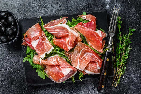 Italiensk parma prosciutto crudo torkad skinka på en marmorbräda. Svart bakgrund. Högst upp. Kopiera utrymme — Stockfoto