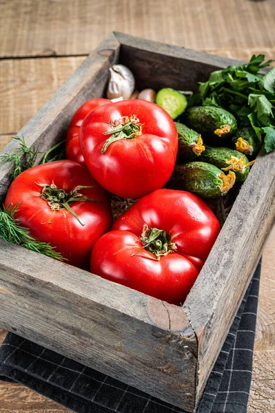 Frisches Gemüse in einer Holzkiste, rote Tomaten, grüne Gurken mit Kräutern. Holzuntergrund. Ansicht von oben — Stockfoto