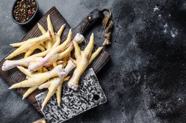 Kasaptaki çiğ tavuk ayakları satırla tahtayı kesiyor. Siyah arka plan. Üst Manzara. Boşluğu kopyala