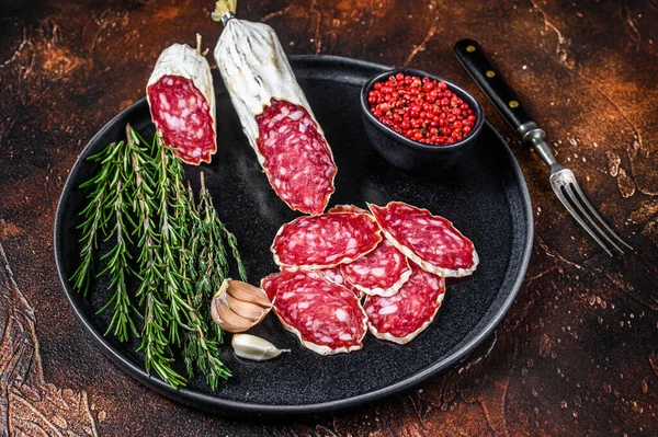 Italiensk skivad salami på en tallrik med rosmarin och timjan. Mörk bakgrund. Ovanifrån — Stockfoto