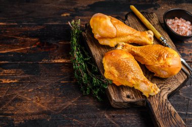 Ahşap kesme tahtasının üzerinde marine edilmiş ve tütsülenmiş tavuk budu budu. Koyu ahşap arka plan. Üst Manzara. Boşluğu kopyala