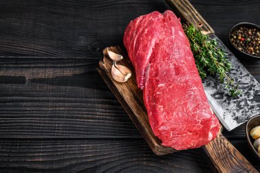 Biftek fileto için çiğ sığır fileto mignon kasap satırıyla ahşap bir kesme tahtasının üzerinde. Siyah ahşap arka plan. Üst Manzara. Boşluğu kopyala