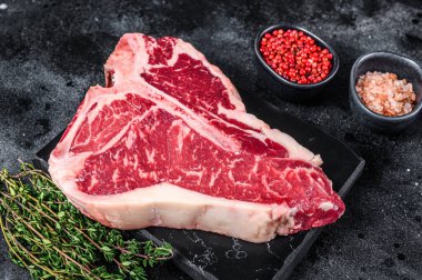 Kurumuş Raw T-bone ya da biftekli biftek, otlar ve tuzlu. Siyah arka plan. Üst görünüm