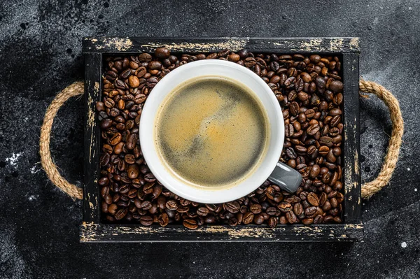 Xícara de café e grãos em bandeja de madeira velha. Fundo preto. Vista superior — Fotografia de Stock