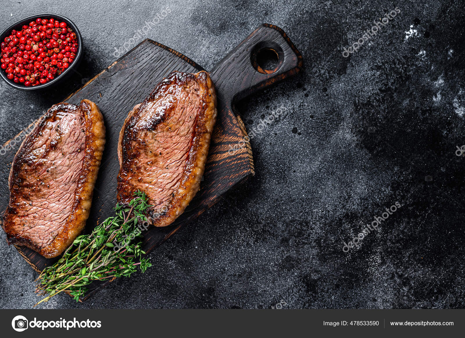 BBQ Grilled top sirloin cap or picanha steak on a wooden cutting board. Black background. Top
