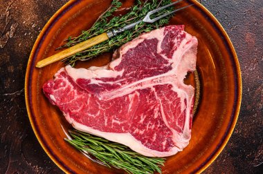 Çiğ biftek bifteği ve tabakta otlar. Karanlık arka plan. Üst görünüm