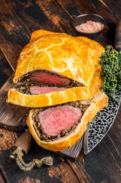 Homemade Beef Wellington puff pie with tenderloin meat on a cutting board. Dark wooden background. Top view