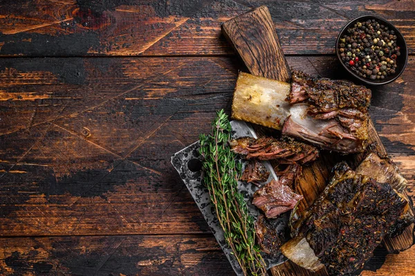 BBQ short chuck beef ribs with herbs and meat cleaver. Dark wooden background. Top view. Copy space