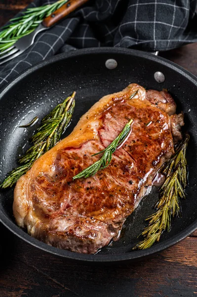 Bifteck de viande de bœuf striploïne grillé dans une casserole avec des herbes. Fond en bois foncé. Vue du dessus — Photo