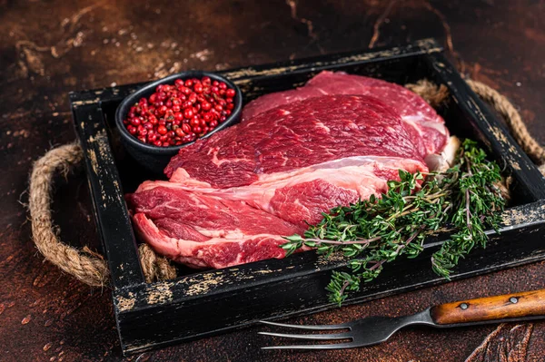 Čerstvé syrové Chuck oko rohlík hovězí steak v dřevěném podnosu s bylinkami. Tmavé pozadí. Horní pohled — Stock fotografie