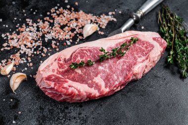 Kasap masasında tuzlu ve kekikli çiğ biftek. Siyah arka plan. Üst görünüm