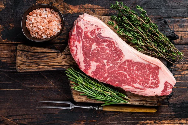 Rauwe steak of striploin op een houten plank. Donker houten achtergrond. Bovenaanzicht — Stockfoto