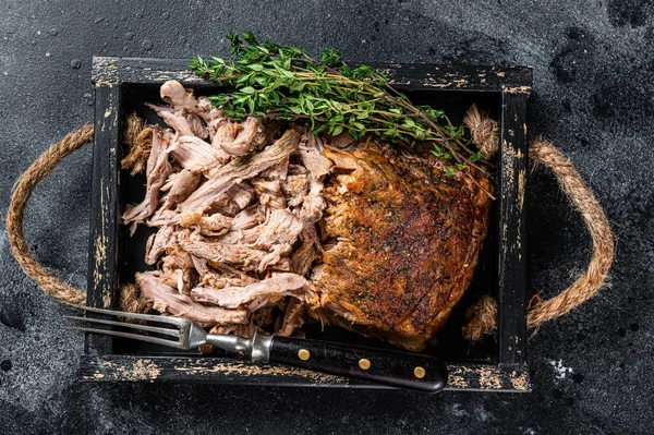 Bbq slow roast puilled pork meat in a wooden tray. Black background. Top view